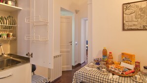 A compact kitchen with a sink, a white door, and a dining area with a table set for breakfast. - Affitta Camere Via Veneto (Rome)