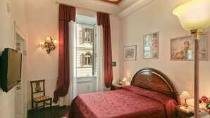 A hotel room with a large bed, a chair, a television, a lamp, and a window with curtains. - Affitta Camere Via Veneto (Rome)