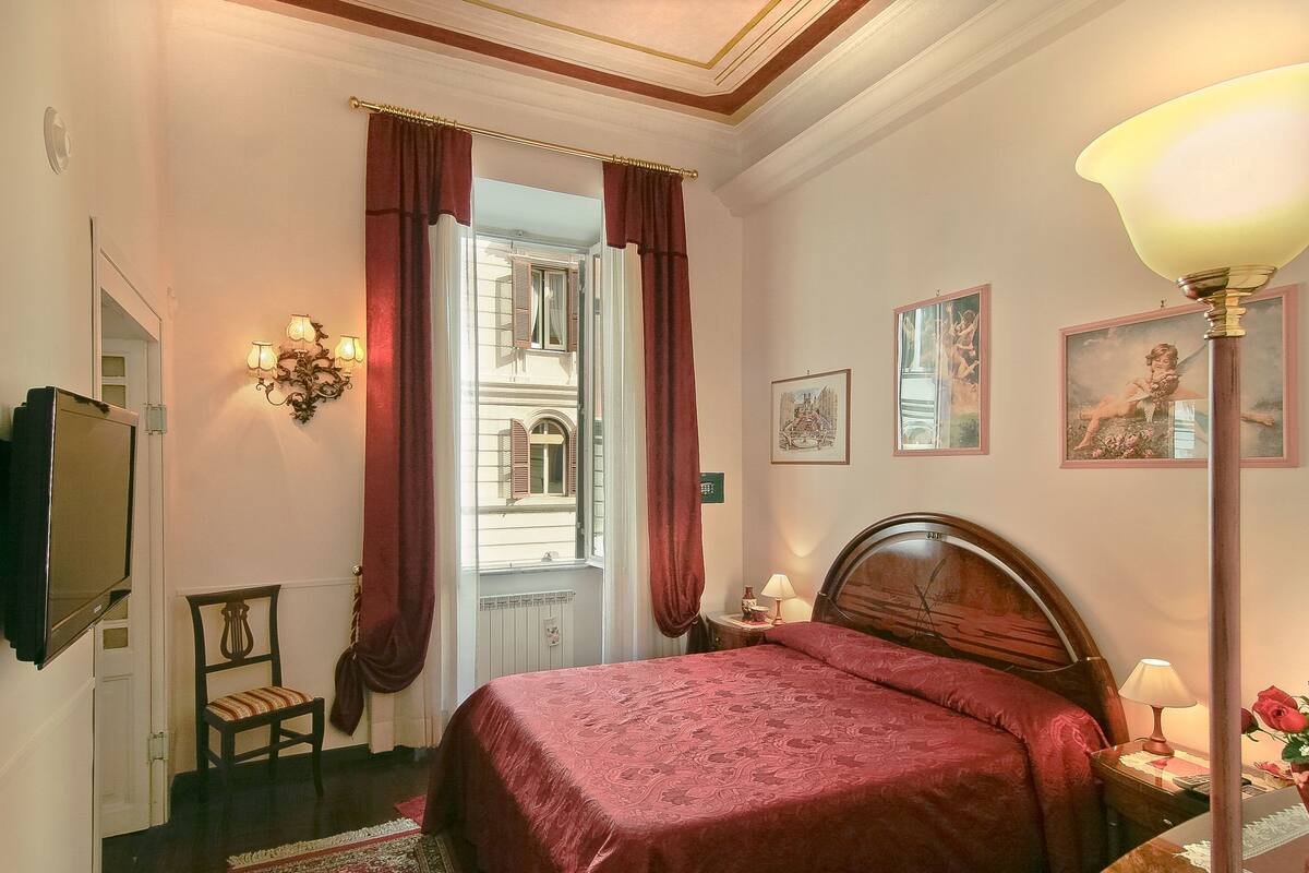 A hotel room with a large bed, a chair, a television, a lamp, and a window with curtains.