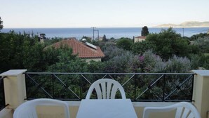 A balcony with a table and chairs overlooking a coastal landscape with houses and vegetation. - Victorias Rooms (Chios)