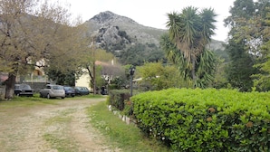 A gravel path leading to parked cars, surrounded by lush greenery and a mountain in the background. - Victorias Rooms (Chios)