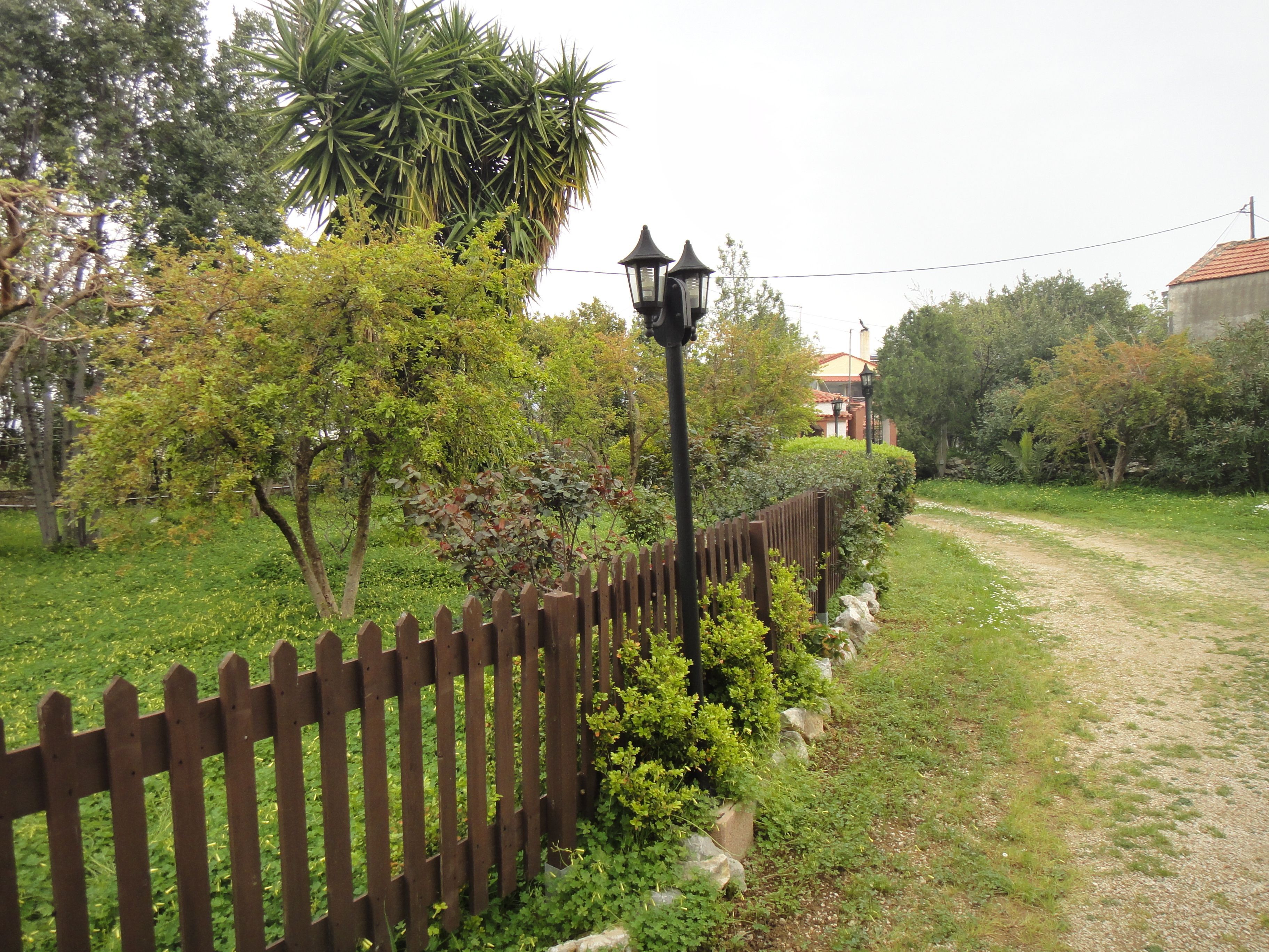 Un jardin entouré d’une clôture en bois, avec un lampadaire et un chemin menant à un bâtiment.