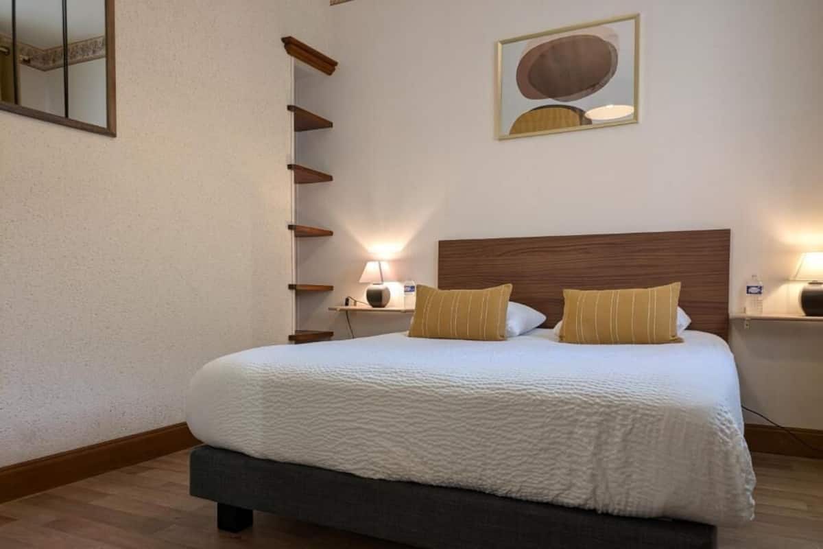 Une chambre à coucher avec un grand lit, deux tables de chevet avec des lampes, une étagère fixée au mur et un tableau au-dessus du lit.