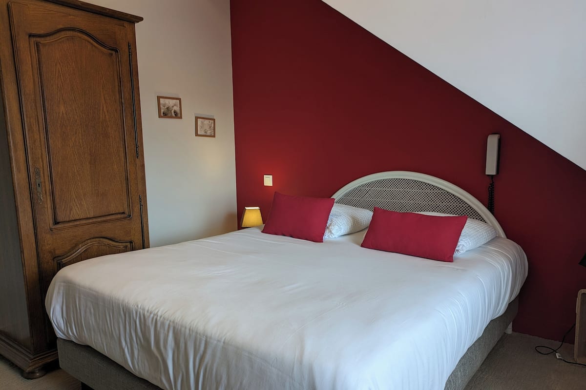 Une chambre à coucher avec un lit, une armoire en bois et un mur d’accent de couleur rouge.