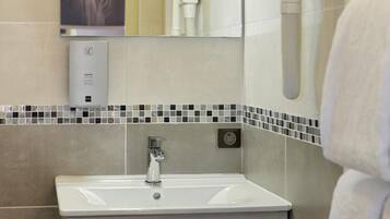 A modern bathroom with a sink, mirror, towel rack, and a soap dispenser.