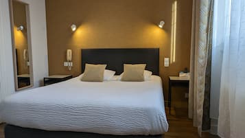 Un lit bien fait, recouvert d’une couette blanche à texture intéressante, avec deux oreillers beige et une tête de lit sombre. De chaque côté du lit, on trouve des tables de chevet avec des lampes, et un téléphone est fixé au mur.
