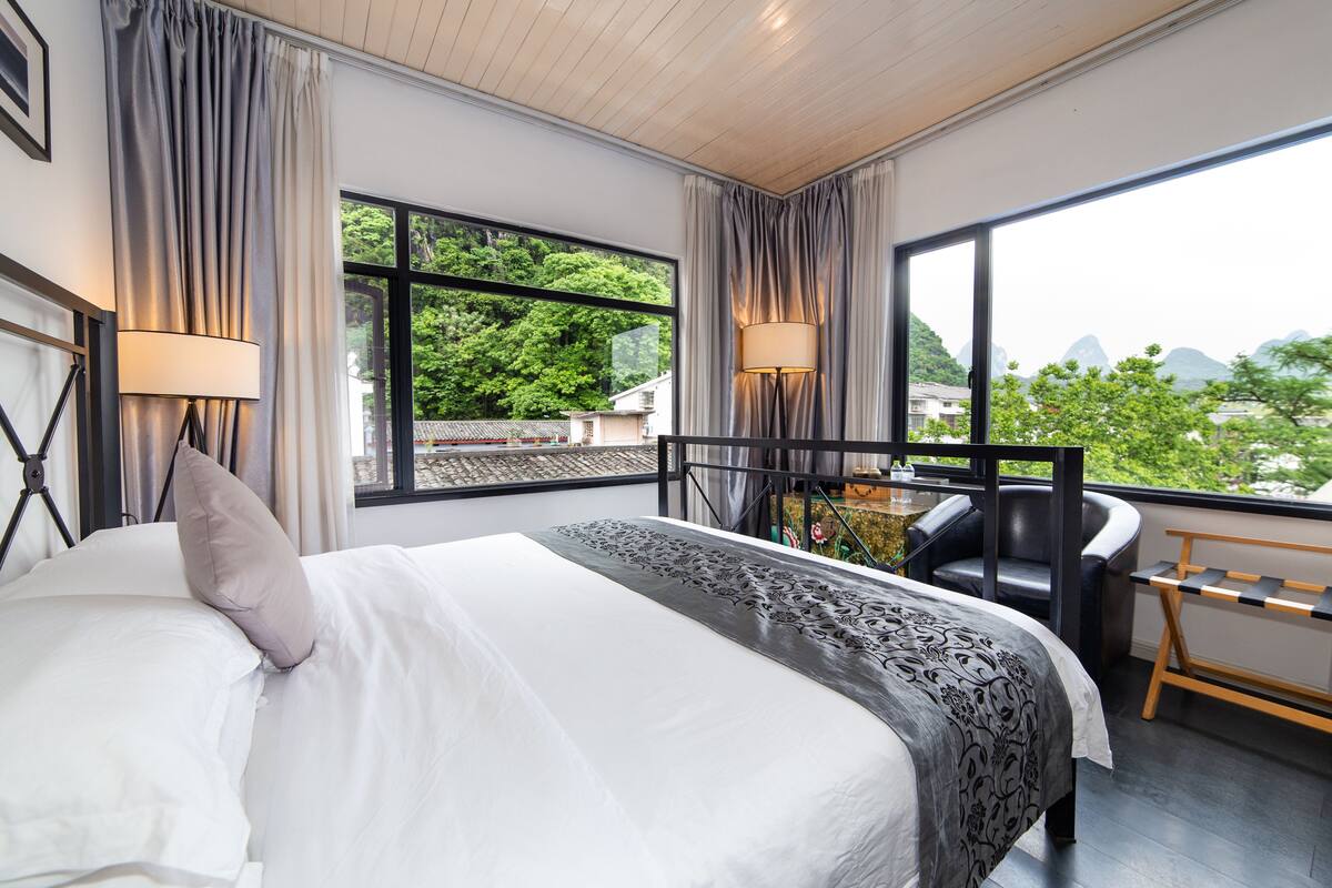Ein Hotelzimmer mit einem großen Bett, einem Schreibtisch und Blick auf Grünflächen und Berge.