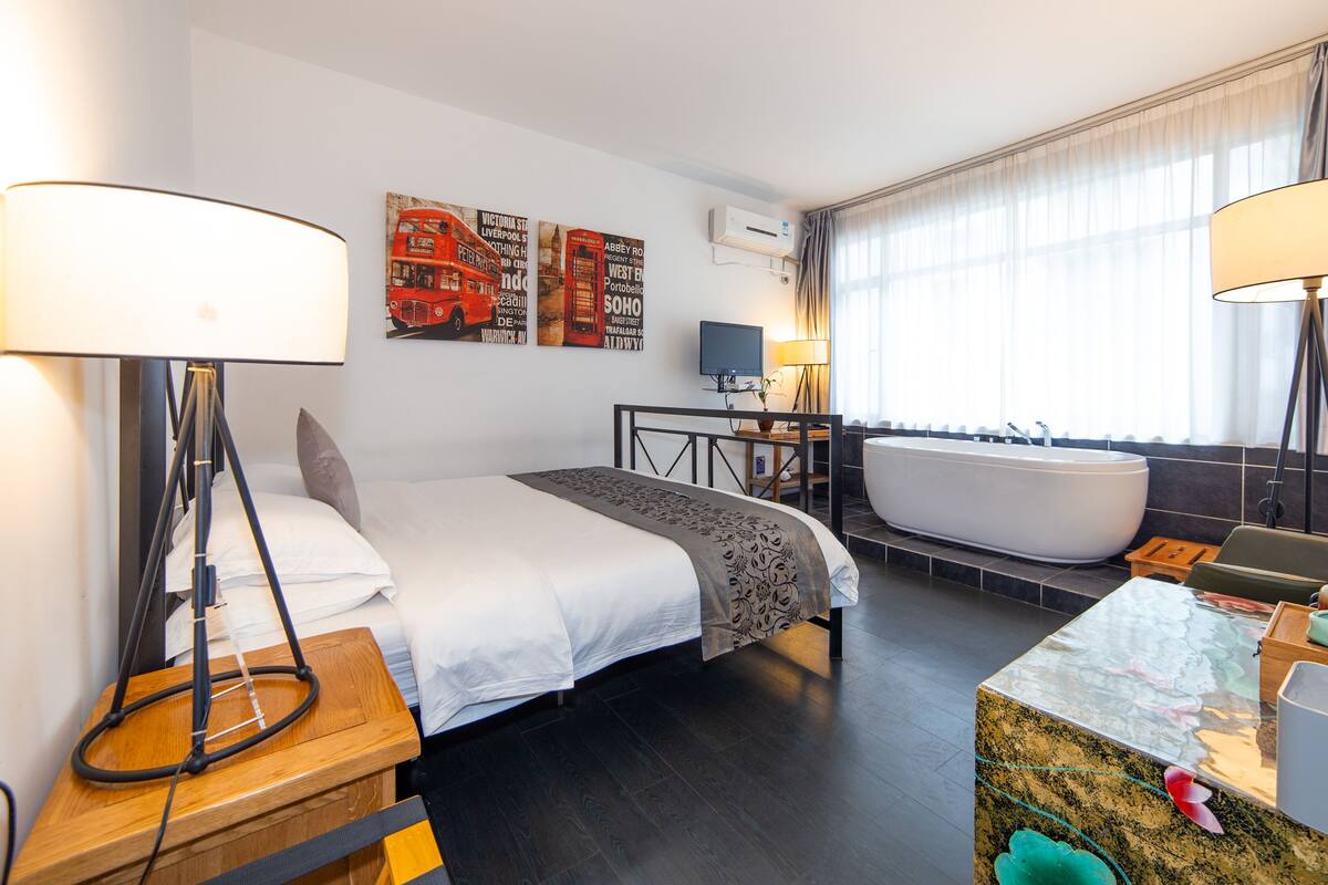 Ein modernes Hotelzimmer mit einem großen Bett, einer Sitzecke mit Schreibtisch, einer Badewanne sowie einem Badezimmer mit Spiegel und Waschbecken.