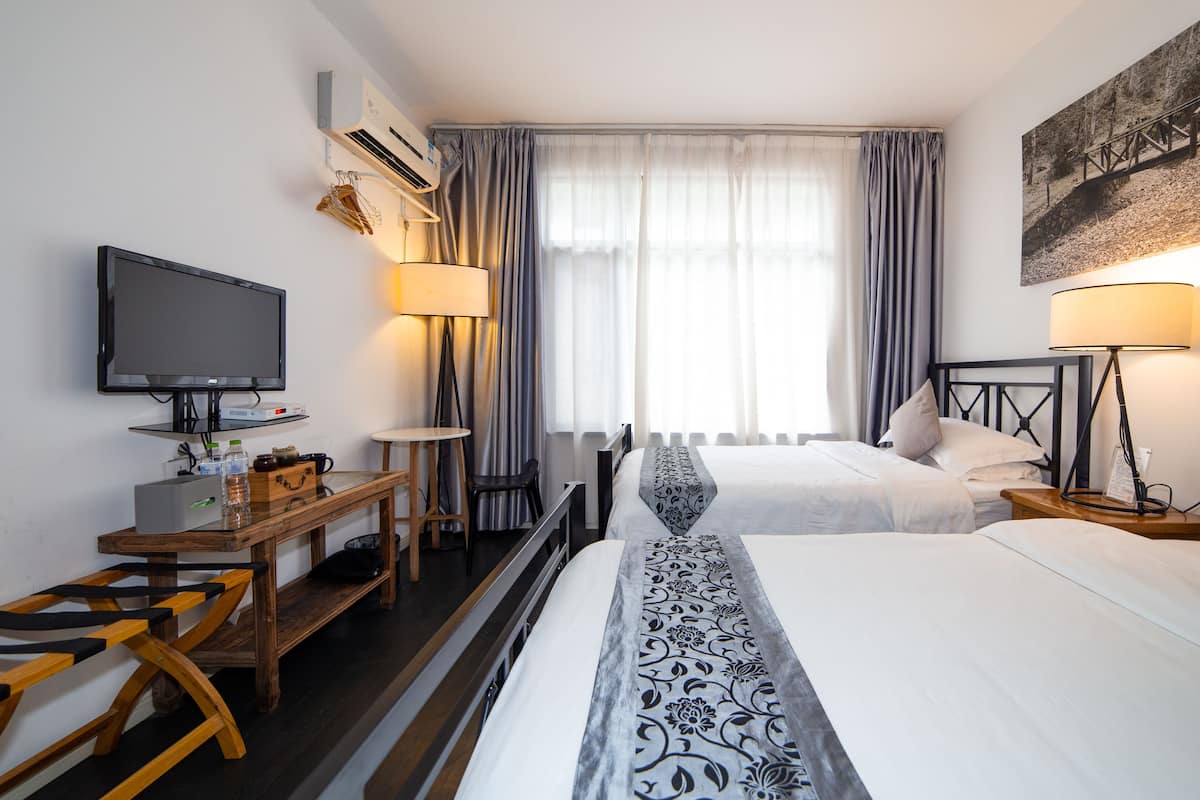 Ein Hotelzimmer mit zwei Betten, einem Schreibtisch, einem Fernseher und einem Fenster mit Vorhängen.