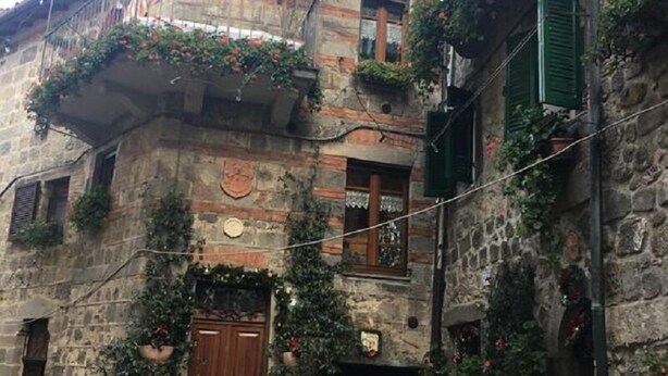 A stone building with a wooden door, potted plants, and green shutters. - Osteria Dei Locandieri (Abbadia San Salvatore)