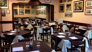 A restaurant interior with tables set for dining, framed artwork on the walls, and a classic interior design. - Osteria Dei Locandieri (Abbadia San Salvatore)