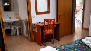 A hotel room with a bed, a desk, a chair, a bathroom with a sink, and a mirror. - Osteria Dei Locandieri (Abbadia San Salvatore)