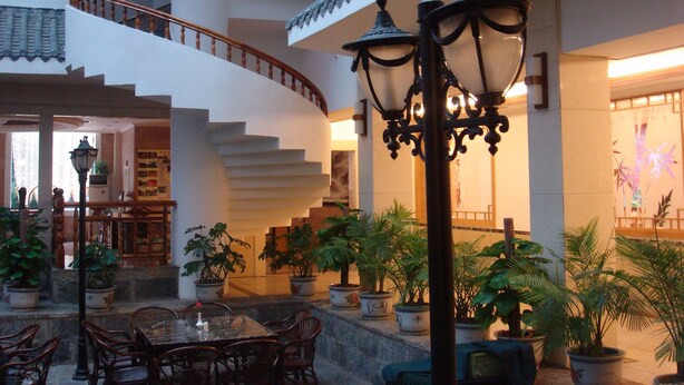 A spacious lobby with a grand staircase, multiple potted plants, and a dining area with wooden furniture. - YangShuo New Century Hotel (Guilin)