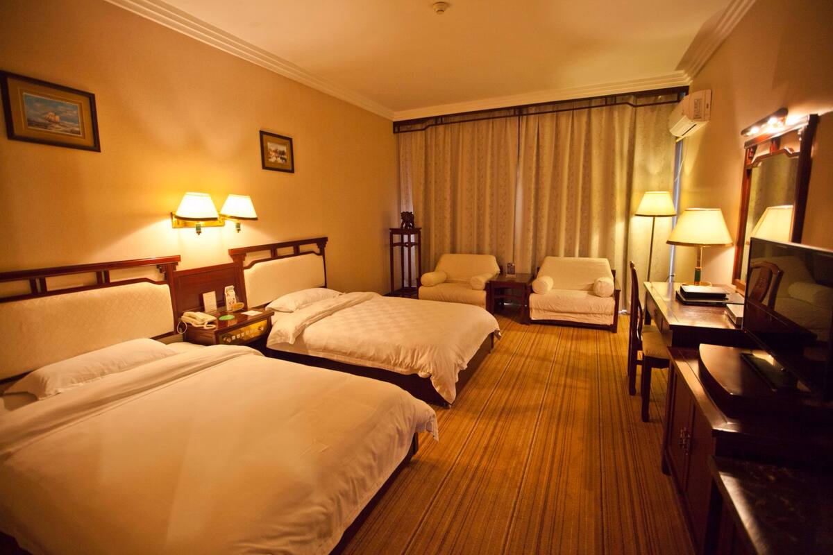 A hotel room with two beds, a desk, a chair, a TV, and a lamp.
