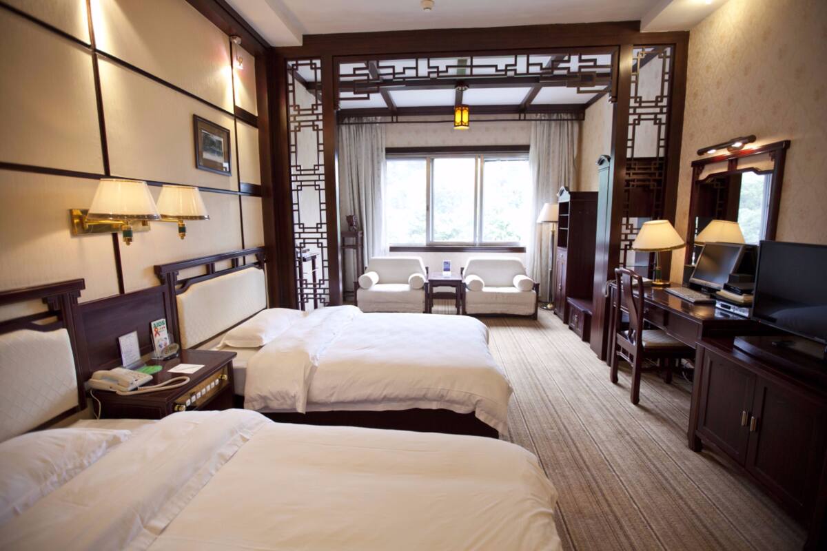 A hotel room with two beds, a desk with a television, a chair, and a window with curtains.