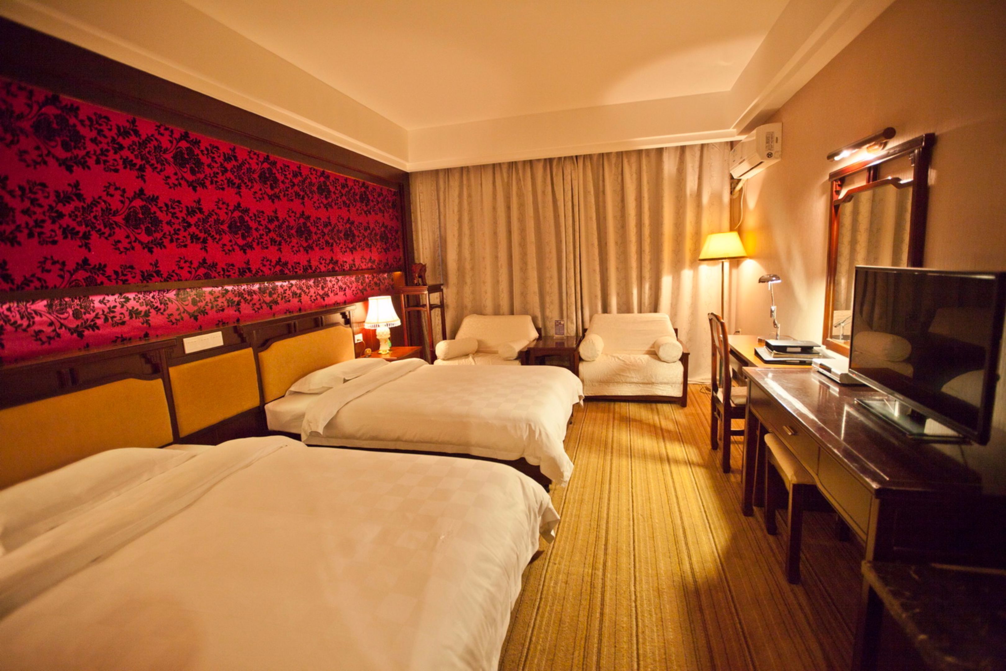 A hotel room with two beds, a desk with a television, a chair, and a large mirror.