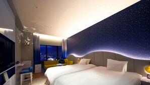 Een moderne hotelkamer met een groot bed, een bureau, een stoel en uitzicht op de stad 's nachts.