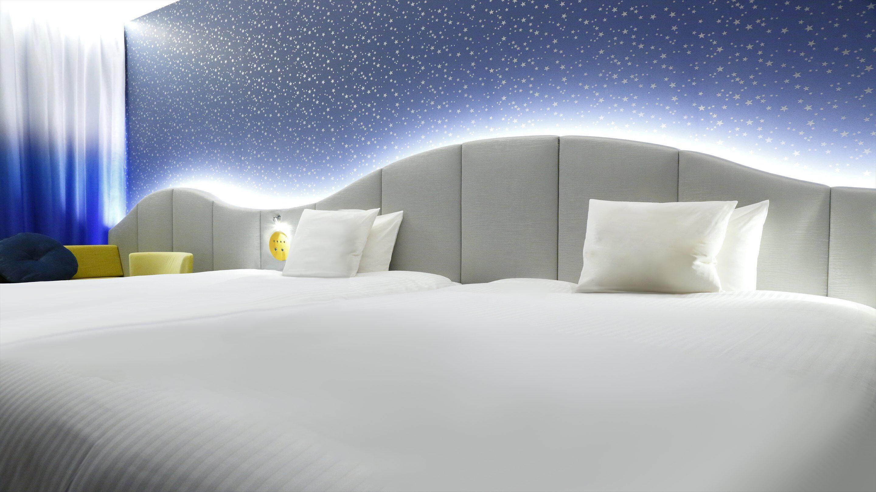 Une chambre d’hôtel avec un lit, des oreillers, une table de chevet et un décor mural représentant un ciel étoilé.