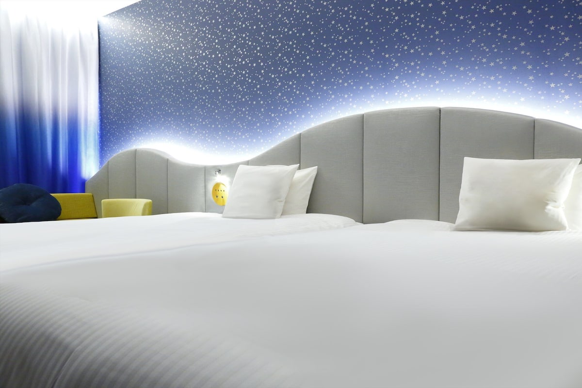 A hotel room with a bed, pillows, a nightstand, and a starry wall design.