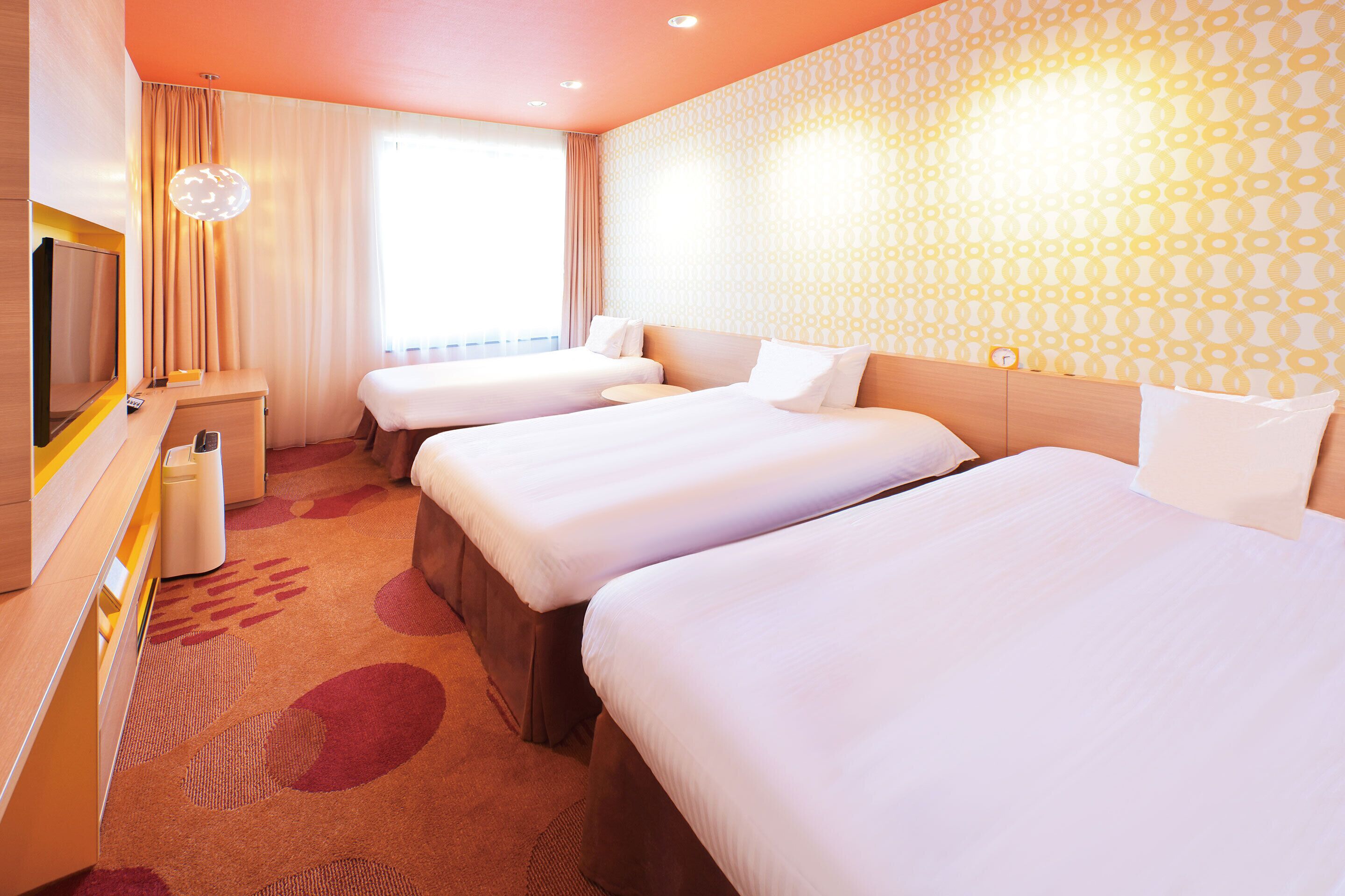 A hotel room with three beds, a TV, a desk, and a trash bin.