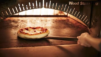 A pizza inside a wood-fired oven with a pizza peel.