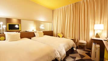 A hotel room with two beds, a desk, a chair, a TV, and a lamp.