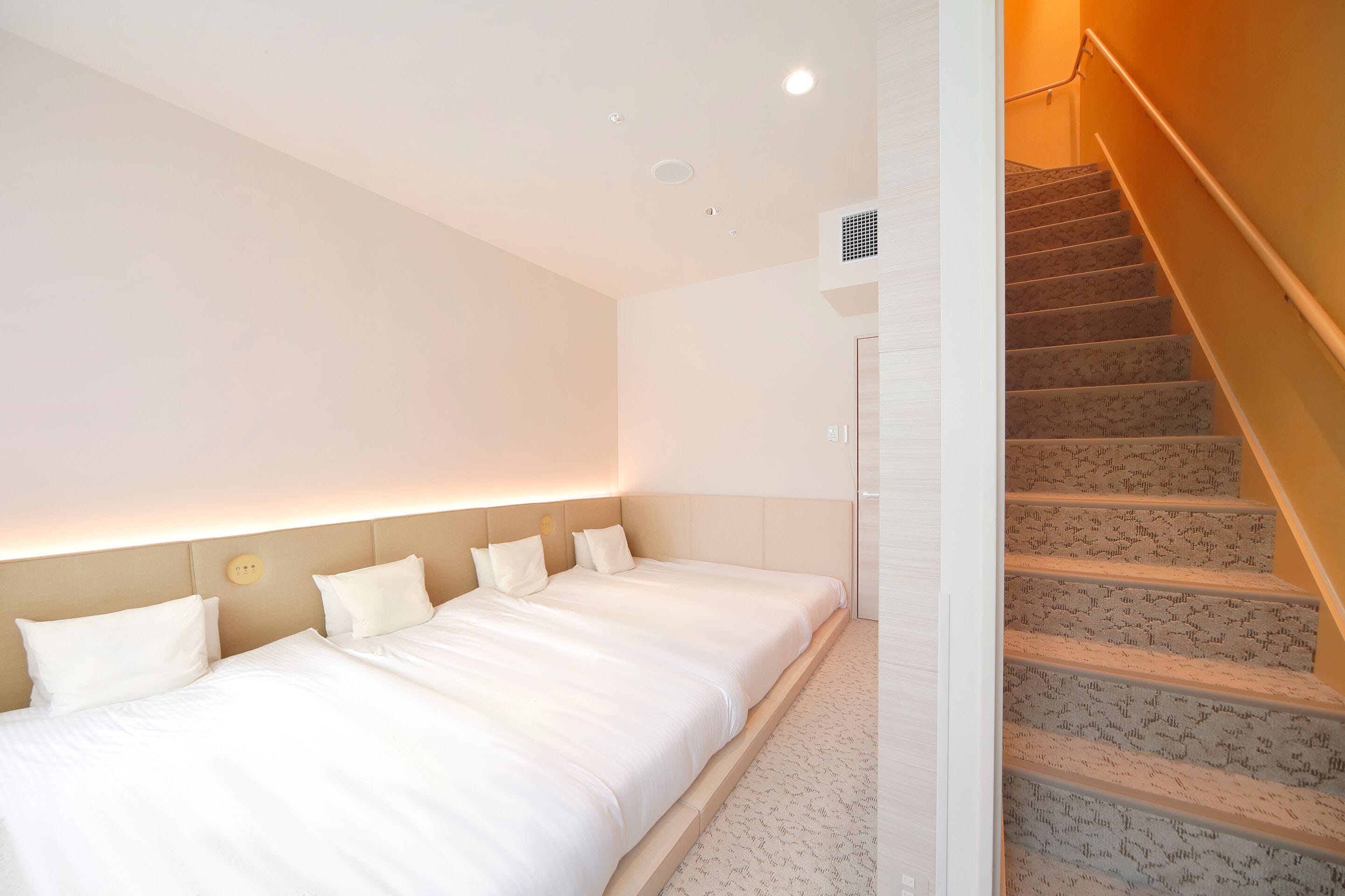 A bedroom with a large bed, a staircase, and a wall-mounted air conditioning unit.