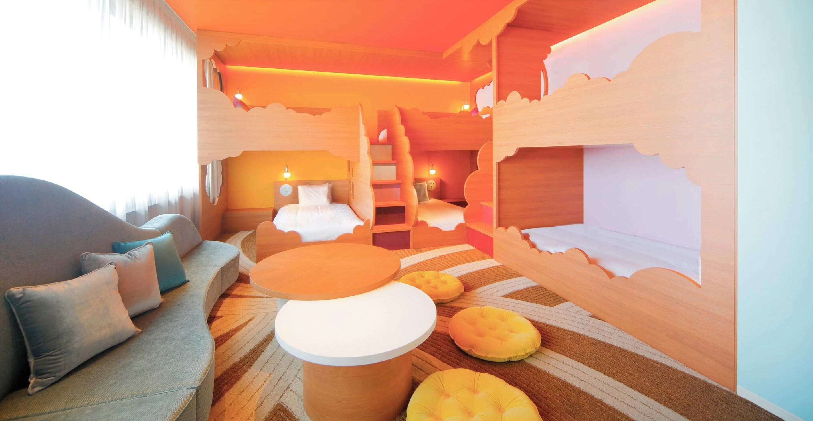 A hotel room with a sofa, ottoman, and a staircase leading to another room.