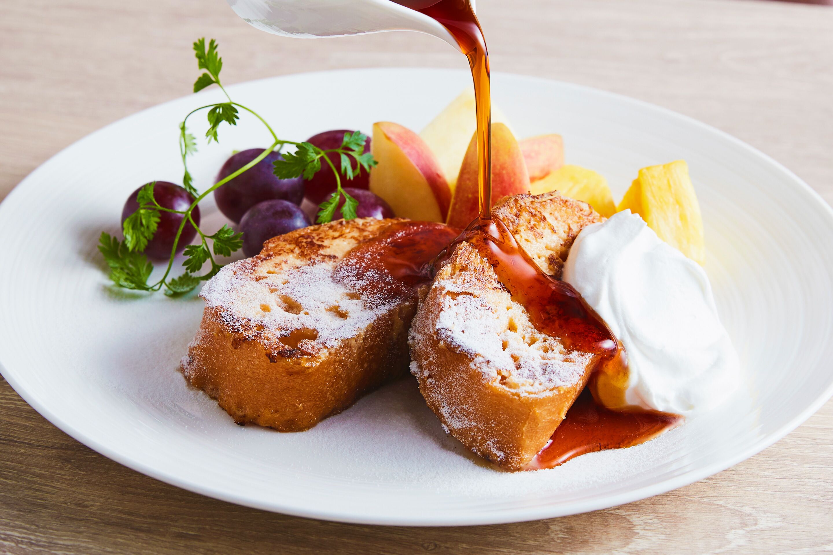 A plate with a dessert consisting of a fruit-topped pastry, a dollop of whipped cream, and a drizzle of syrup.