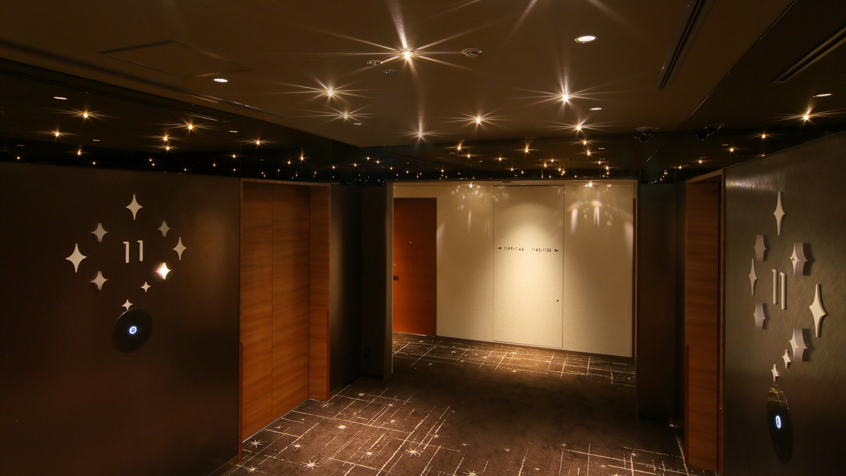 A hallway with star-shaped light fixtures on the ceiling, wooden walls, and a carpet with a star pattern.
