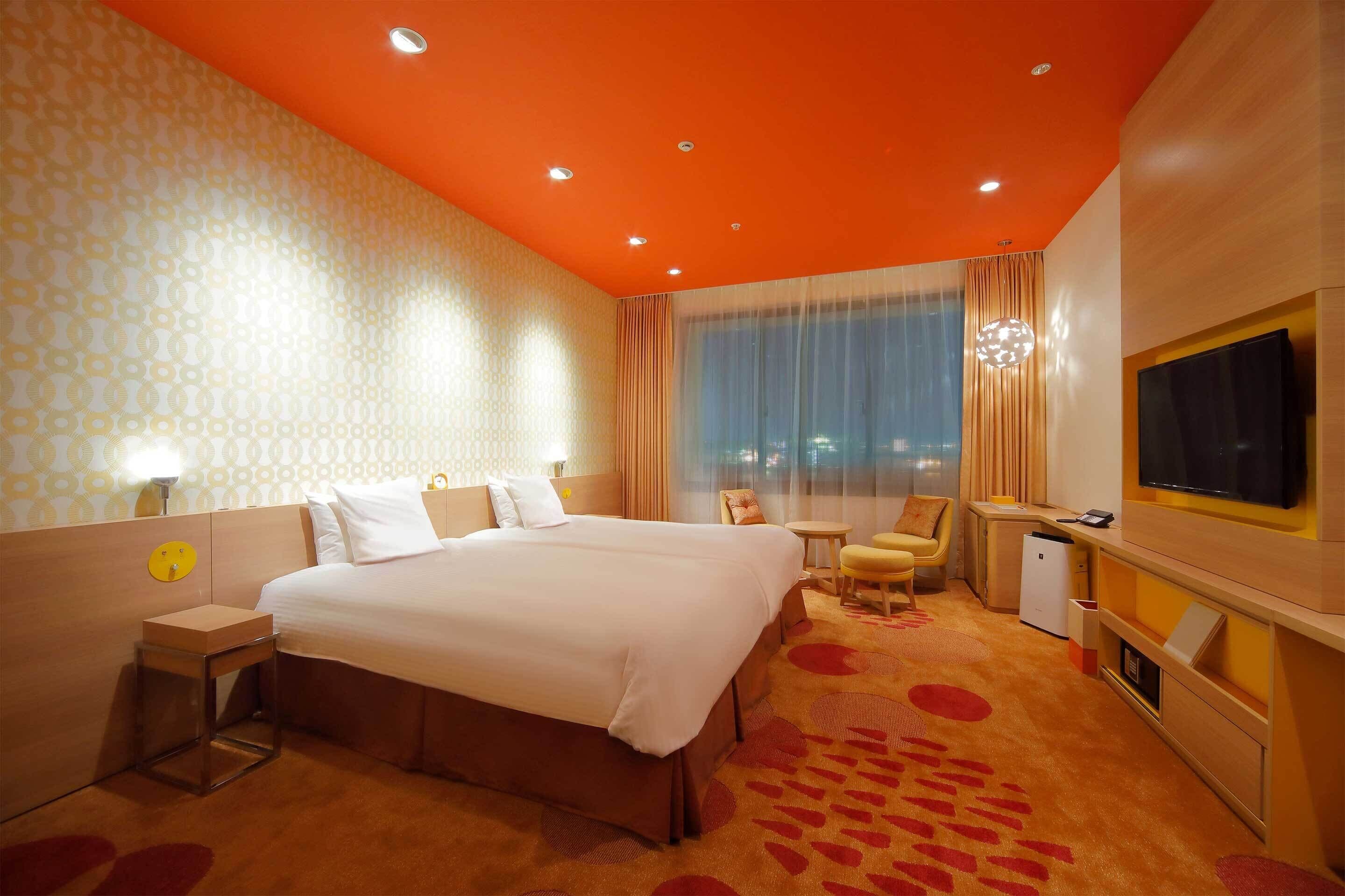 A hotel room with a large bed, a desk, a chair, a TV, and a window with curtains.