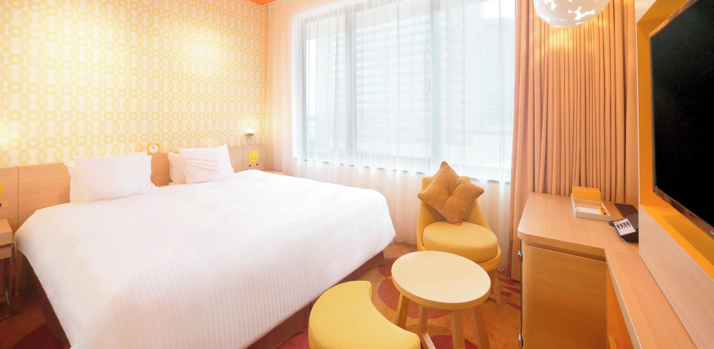 A hotel room with a large bed, a small table, a chair, a TV, and a window with curtains.