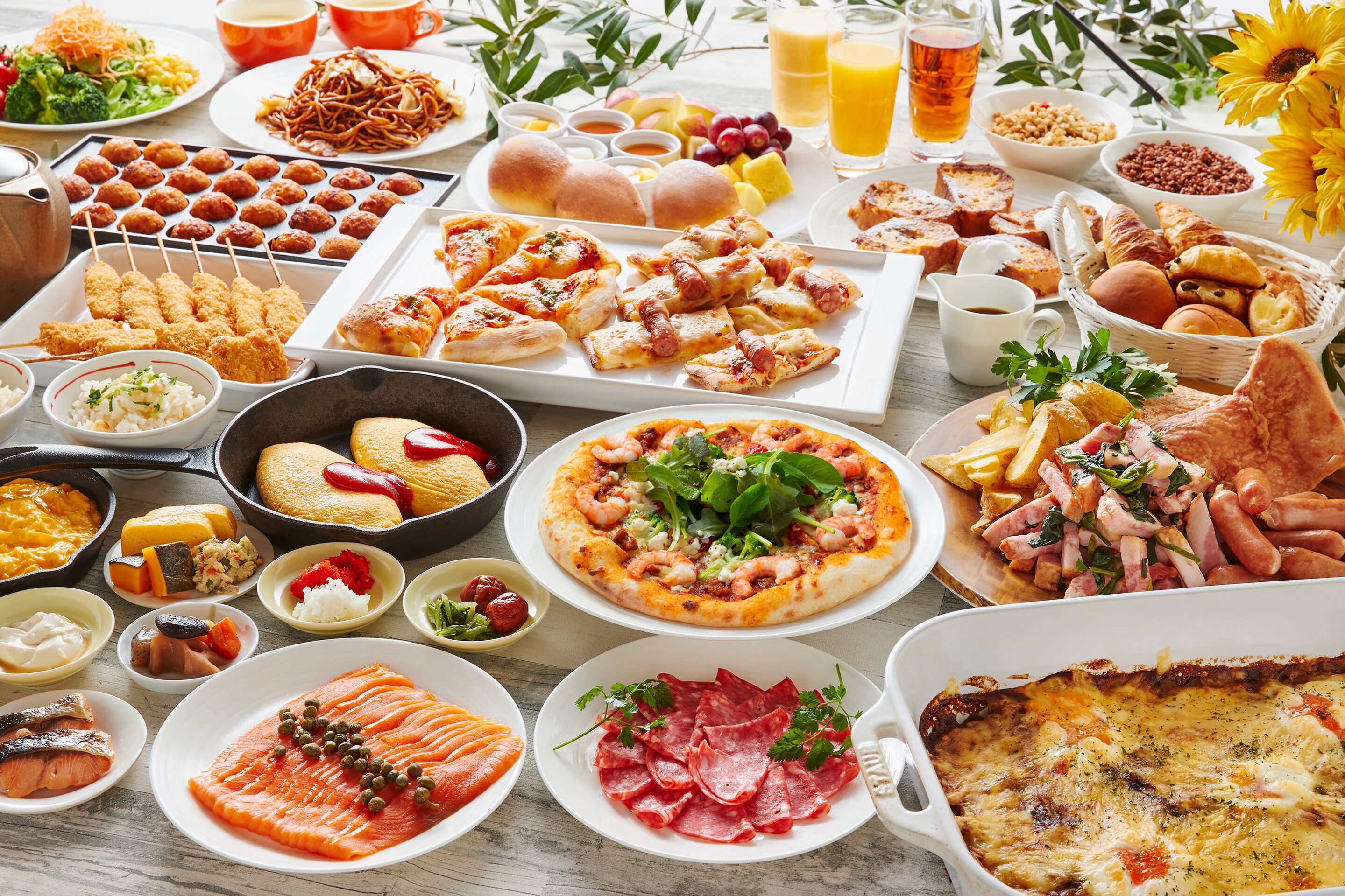 Variedad de alimentos como pizza, salmón y pasteles sobre una mesa.