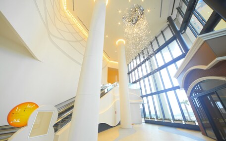 Un interior moderno con una escalera mecánica central, amplios ventanales de vidrio y un candelabro decorativo.