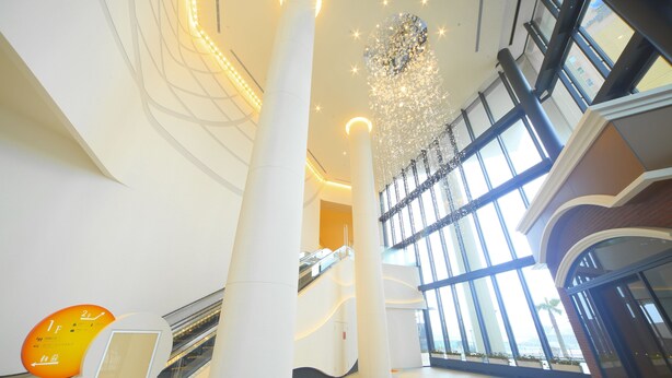 Een modern interieur met een centrale roltrap, grote glasramen en een decoratieve kroonluchter.