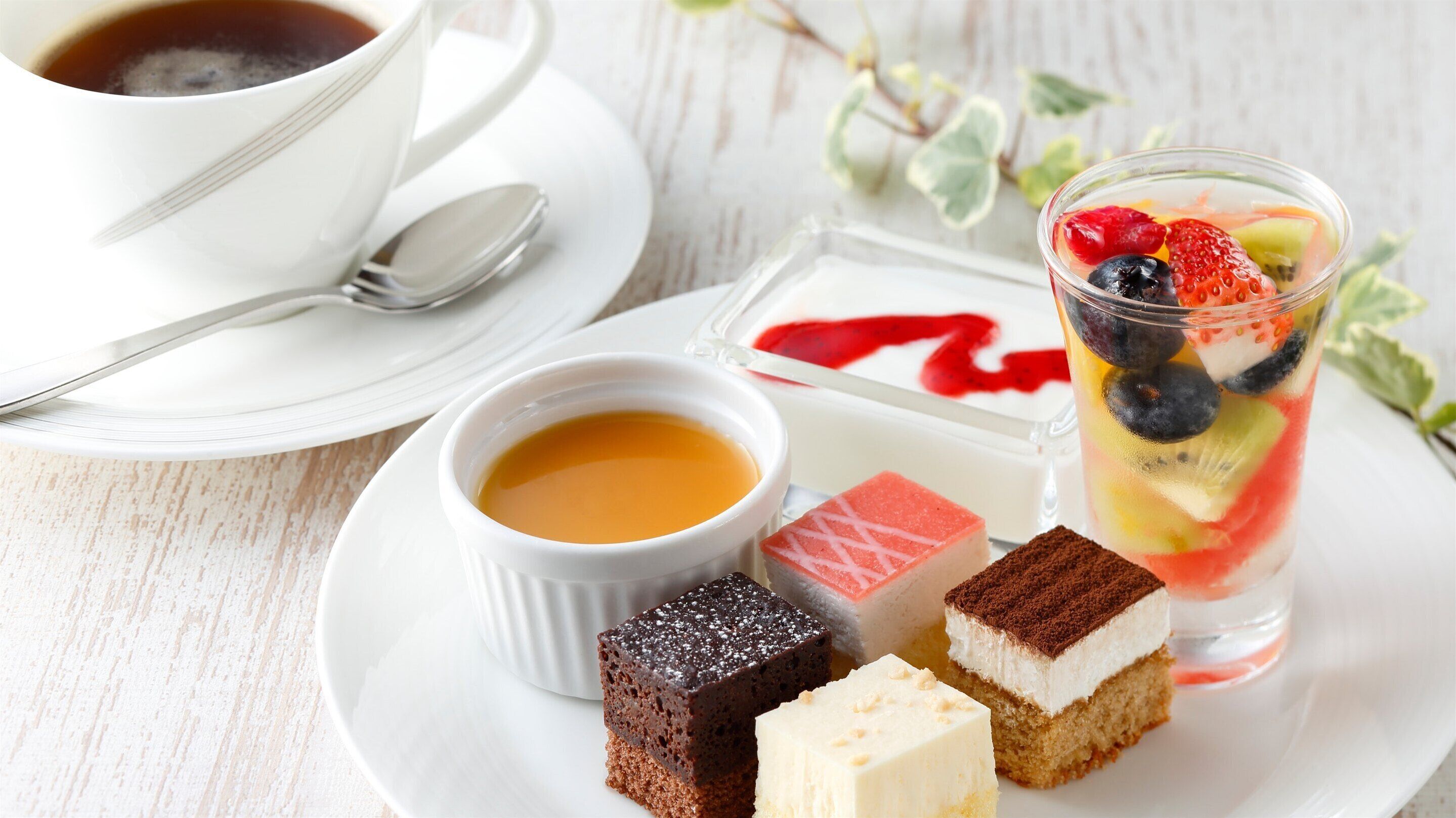 A dessert plate with various cakes and a glass of fruit salad.