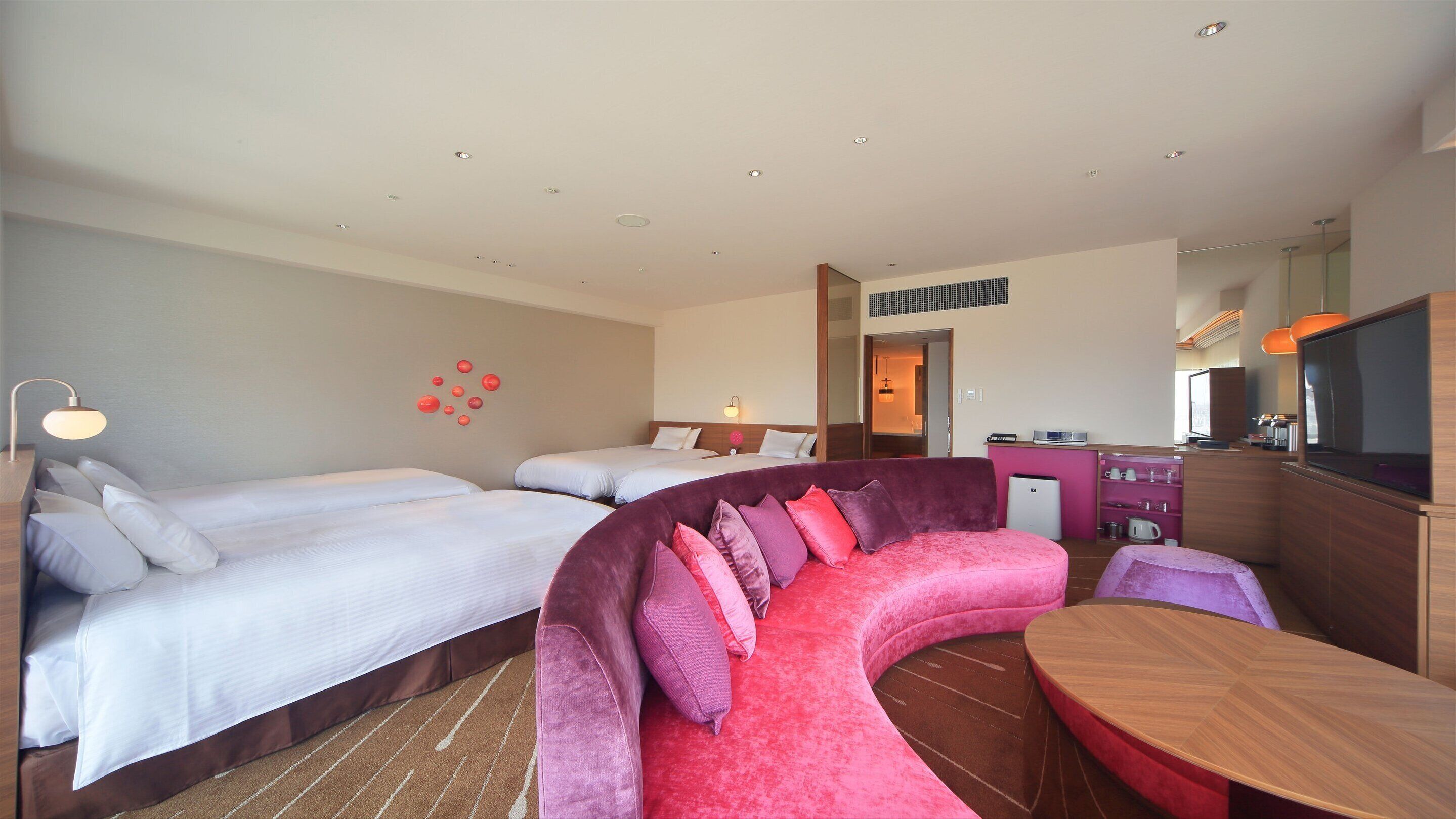 A hotel room with two beds, a sofa, a dining table, and a kitchenette.