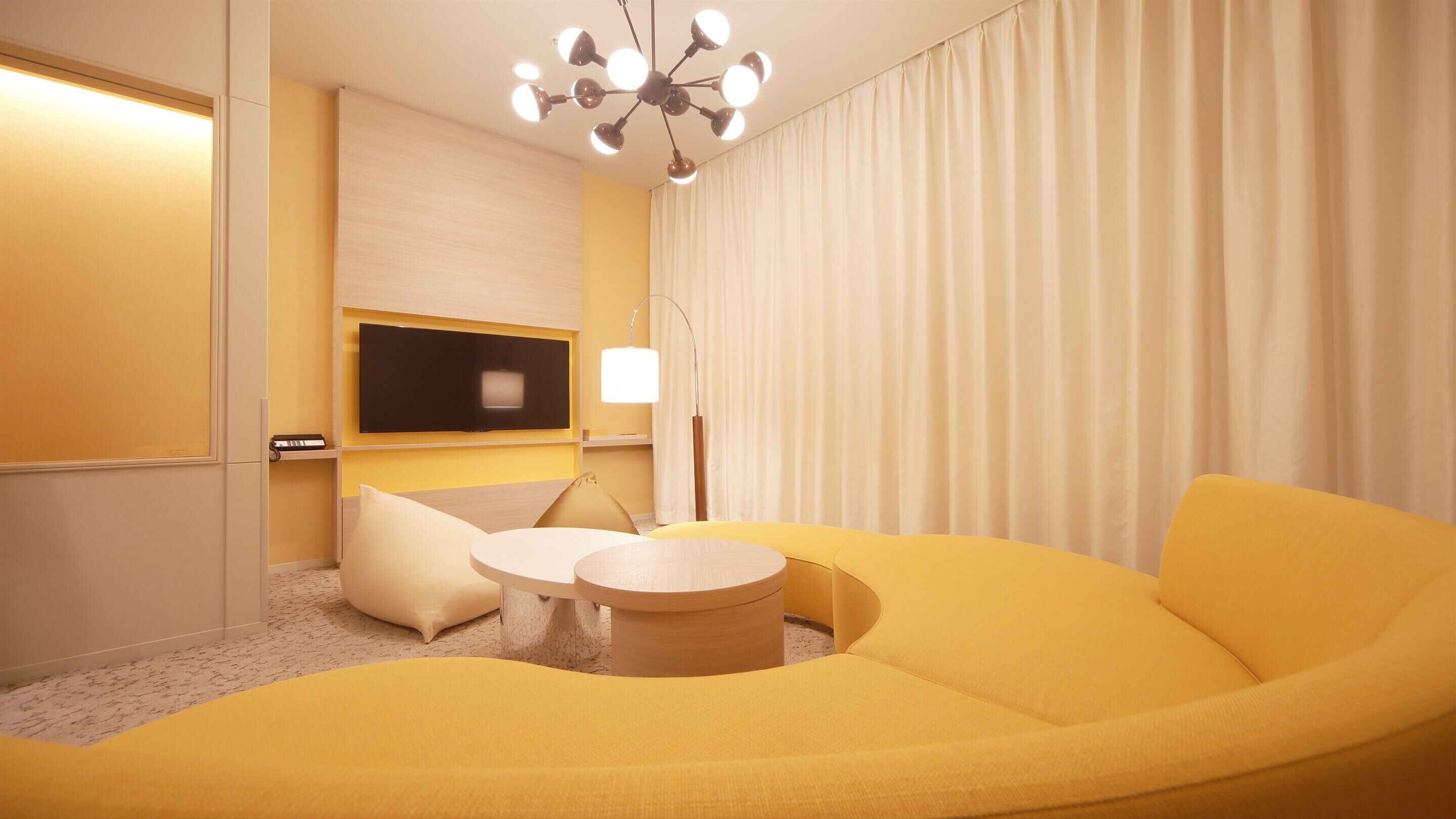 A modern living room with a yellow sofa, a round coffee table, and a flat-screen TV mounted on the wall.