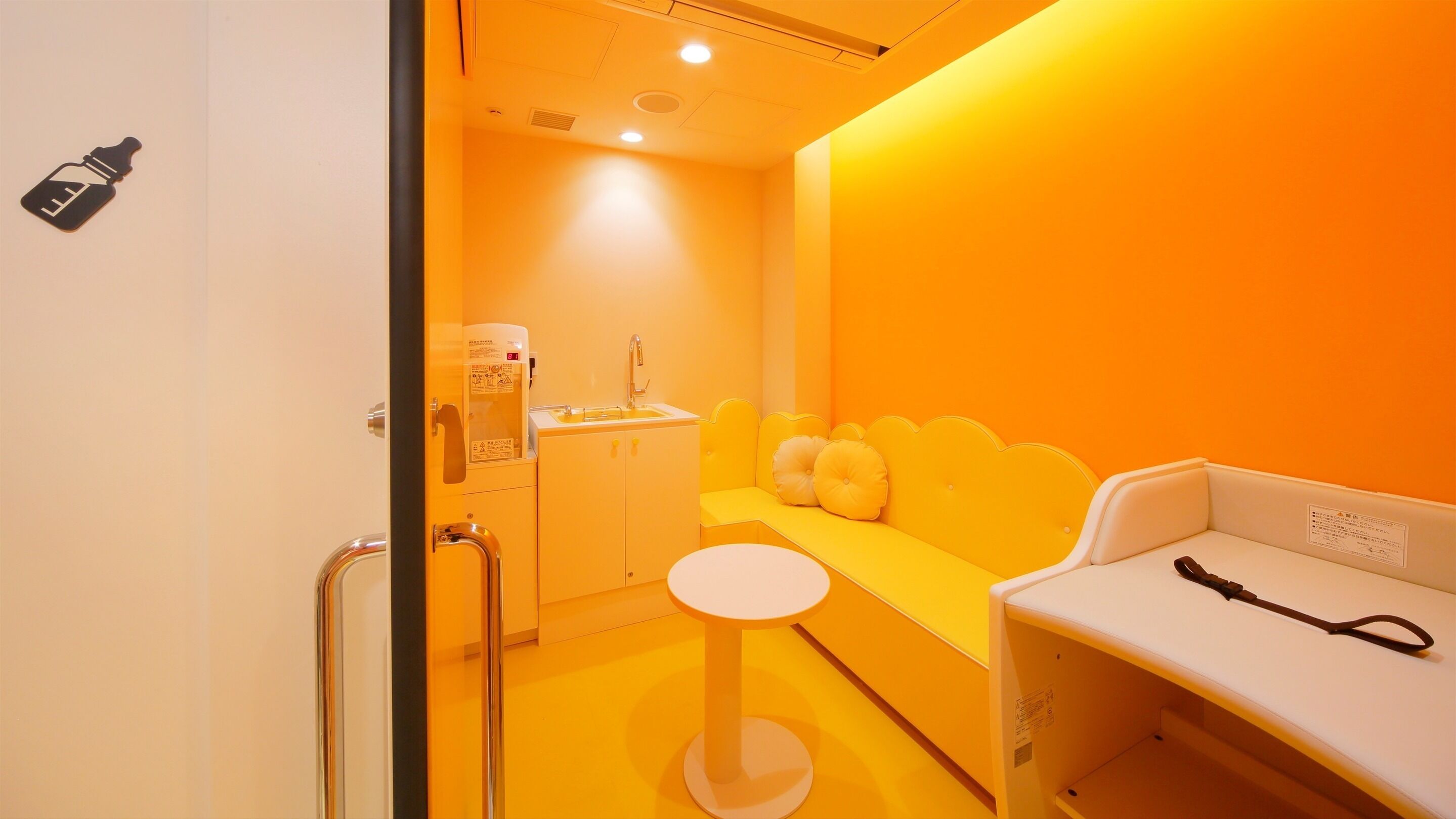 Una habitación con un sofá amarillo, una mesita blanca, un lavabo y una silla con un teléfono.