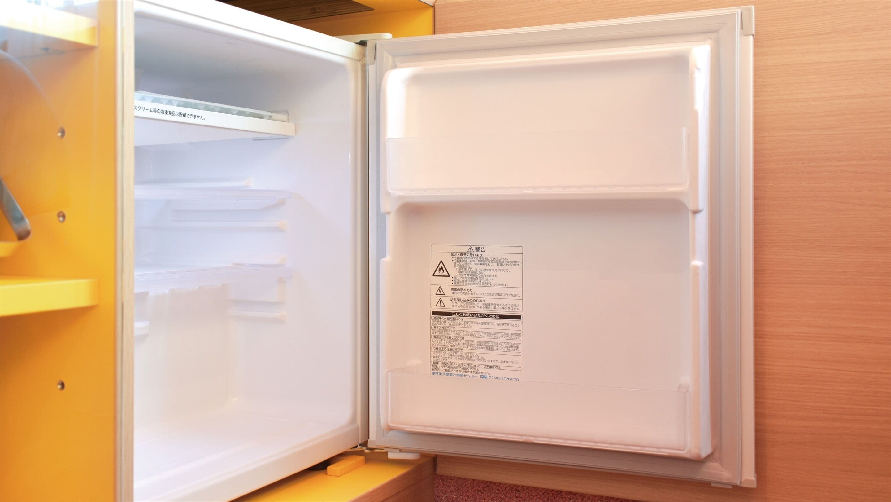 An open refrigerator with a label on the door, a yellow shelf, and a wooden cabinet.