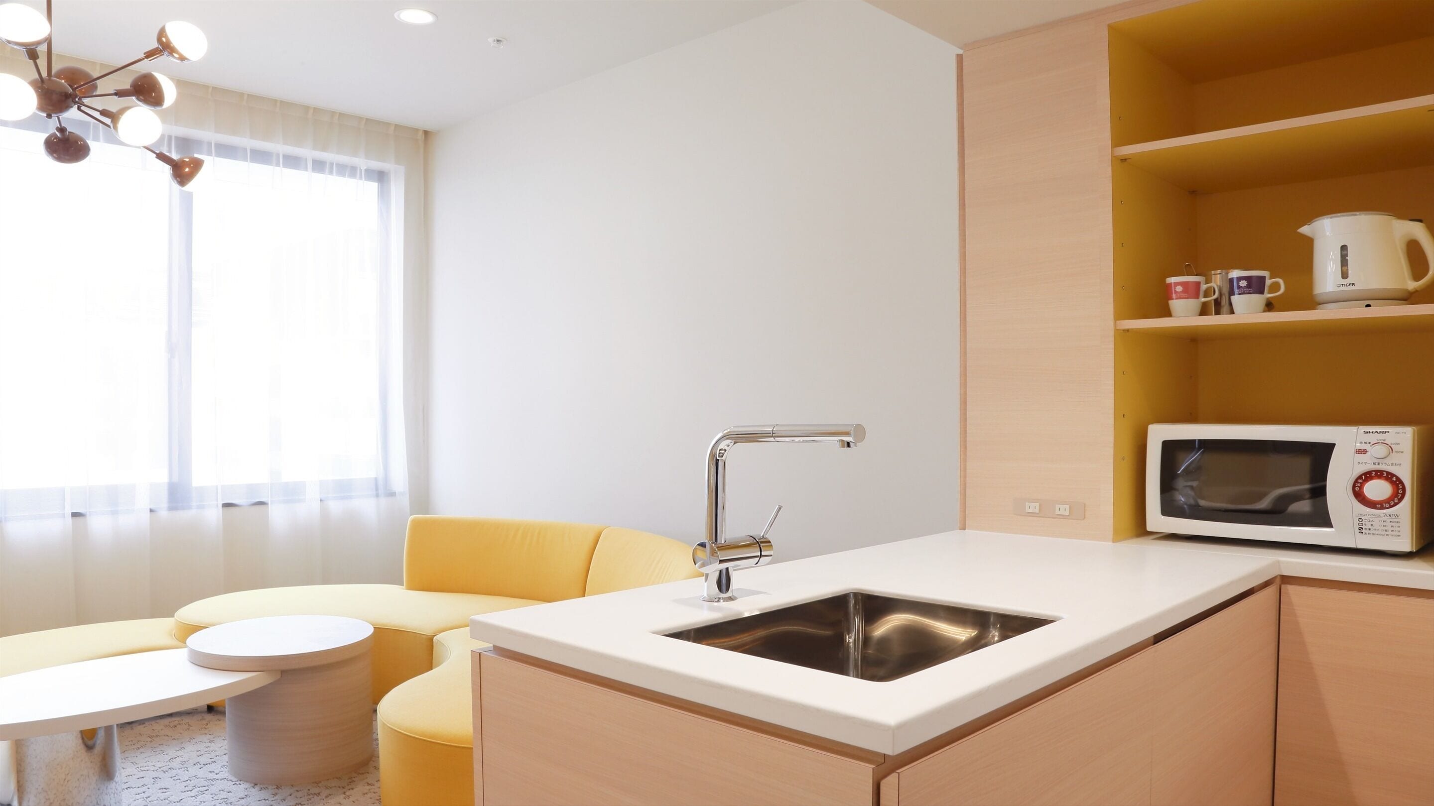 A compact kitchenette with a sink, a microwave, and a small dining area with a yellow sofa and a round table.