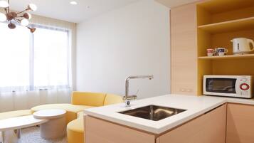 A compact kitchenette with a sink, a microwave, and a small dining area with a yellow sofa and a round table.