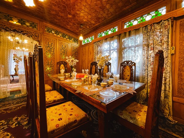 A traditional dining room with a long table set for a meal, surrounded by ornate chairs and floral decorations. - Gemini Group Of Houseboats (Srinagar)