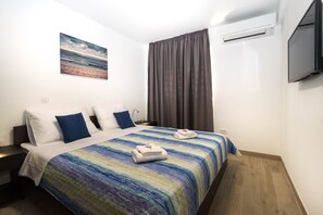 A hotel room with a bed, a nightstand, a TV, and an air conditioning unit. - Amazing Apartments near Center & Beaches (Split)