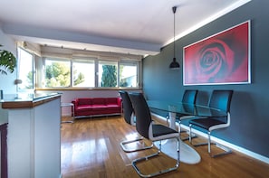 Een moderne vergaderruimte met een glazen tafel, zwart-witte stoelen, een rode bank en een groot abstract schilderij aan de muur.