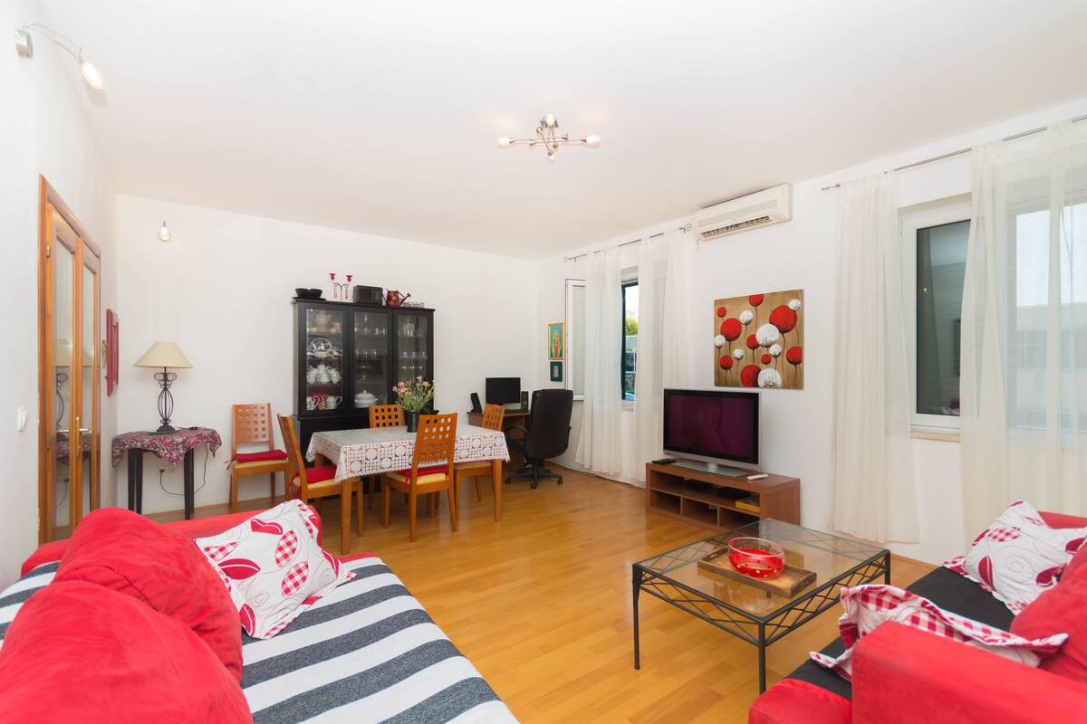 A living room with a sofa, a dining table with chairs, a TV, and a cabinet.