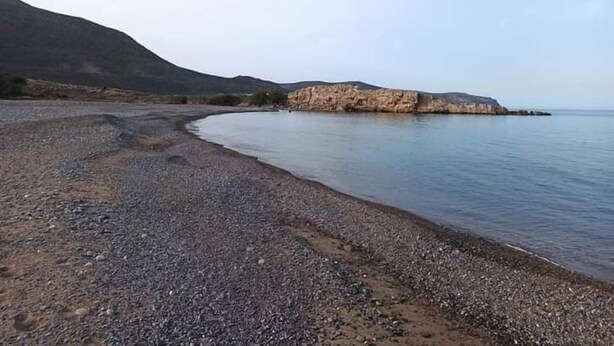 Una playa pedregosa con un promontorio rocoso a lo lejos.