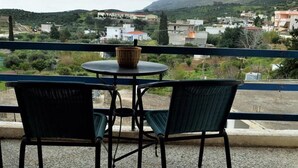 Un balcón con dos sillas de mimbre y una pequeña mesa redonda, con vista a una zona residencial con casas y vegetación.