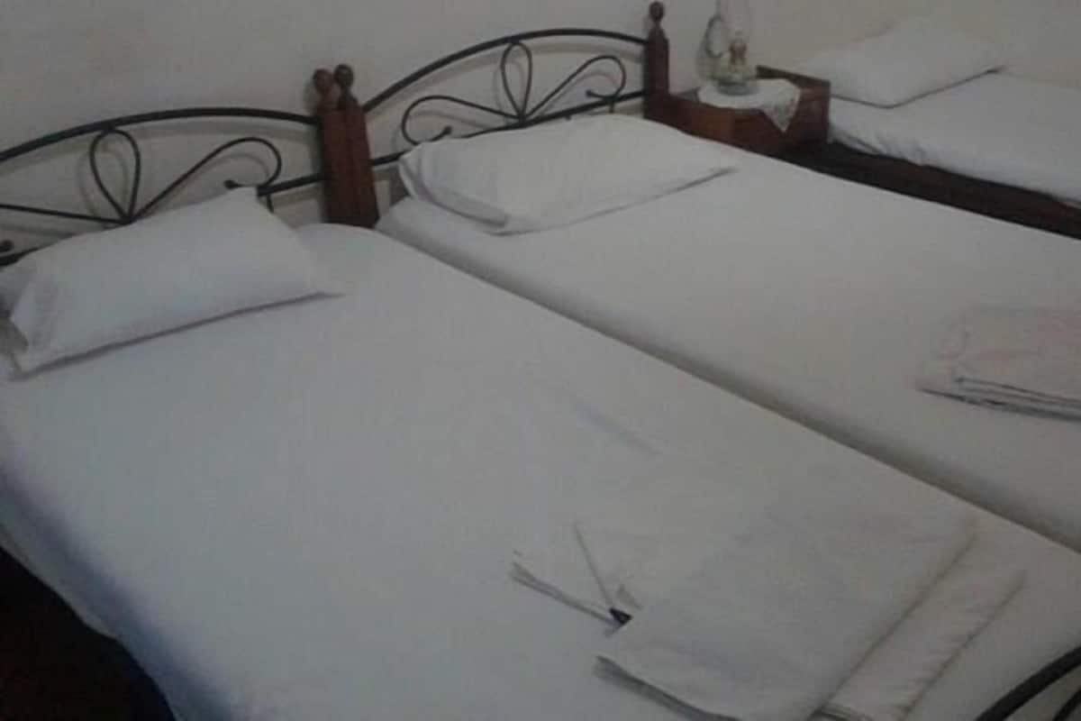 A room with three single beds, each with white bedding and a wooden headboard.