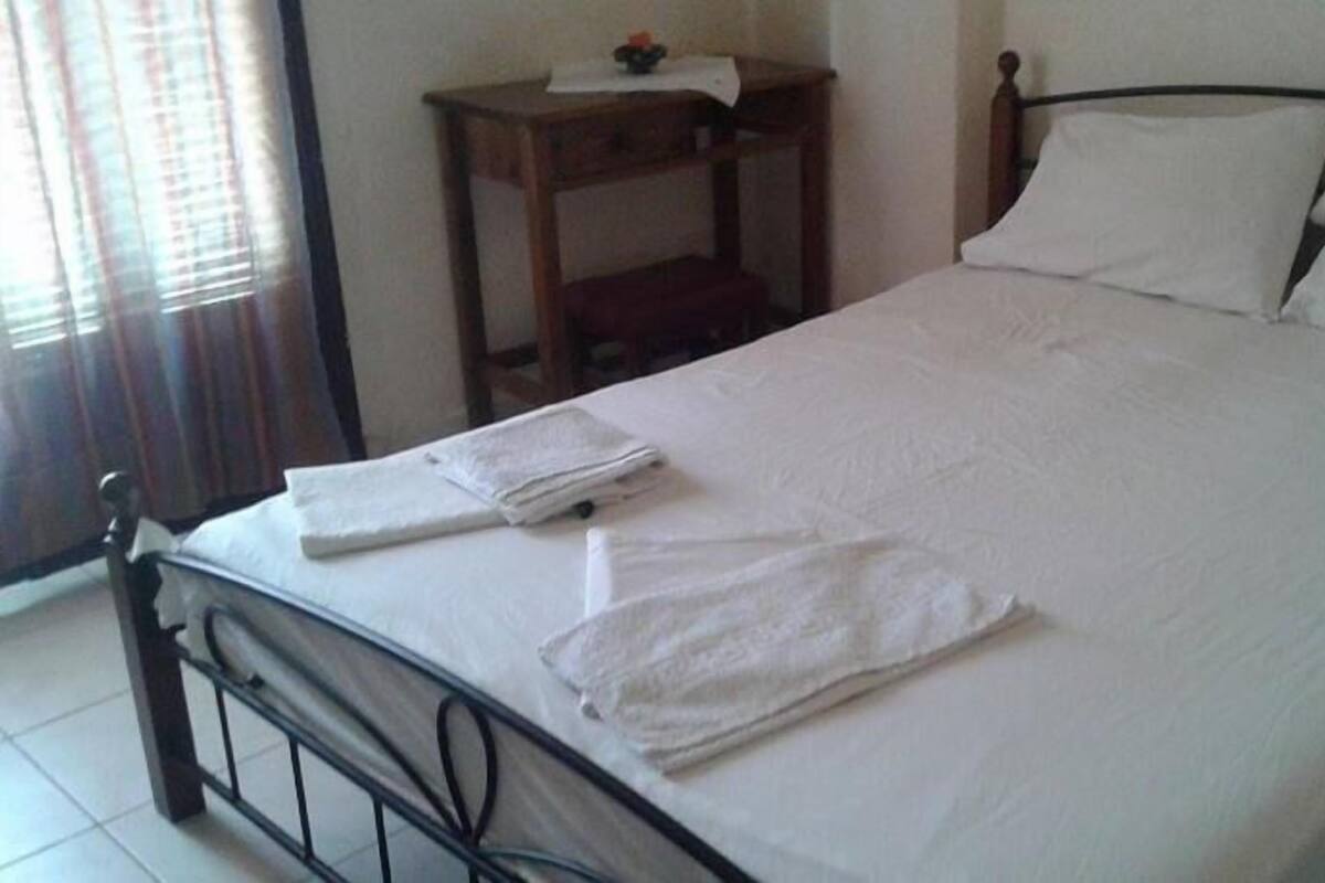 A neatly made bed with white linens and two folded towels on the bed.